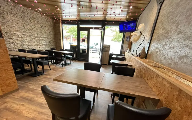 La salle du restaurant : tables en bois, mur de pierre et pluie de pétales roses au plafond
